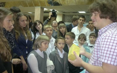 Главный экскурсовод выставки показывает ребятам кирпич будущего  Смотрите, это - НАНО!